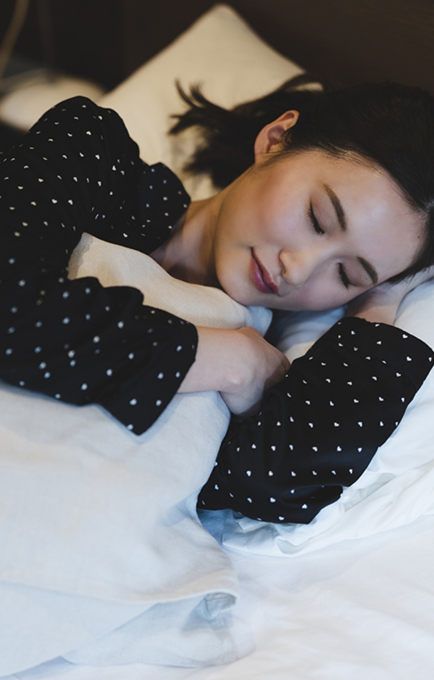 ベッドの中で横向きに眠る女性の写真
